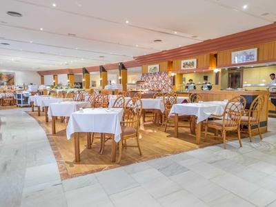 Velká hotelová restaurace s bílými ubrusy a dřevěnými židlemi za teplého osvětlení.