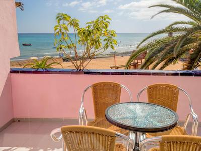 Balkon s kulatým stolem a židlemi, výhled na pláž, moře a palmy za slunečného dne.