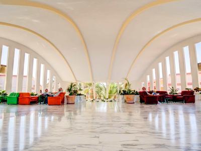 Prostorná hotelová hala s vysokými obloukovými okny a barevnými posezeními.