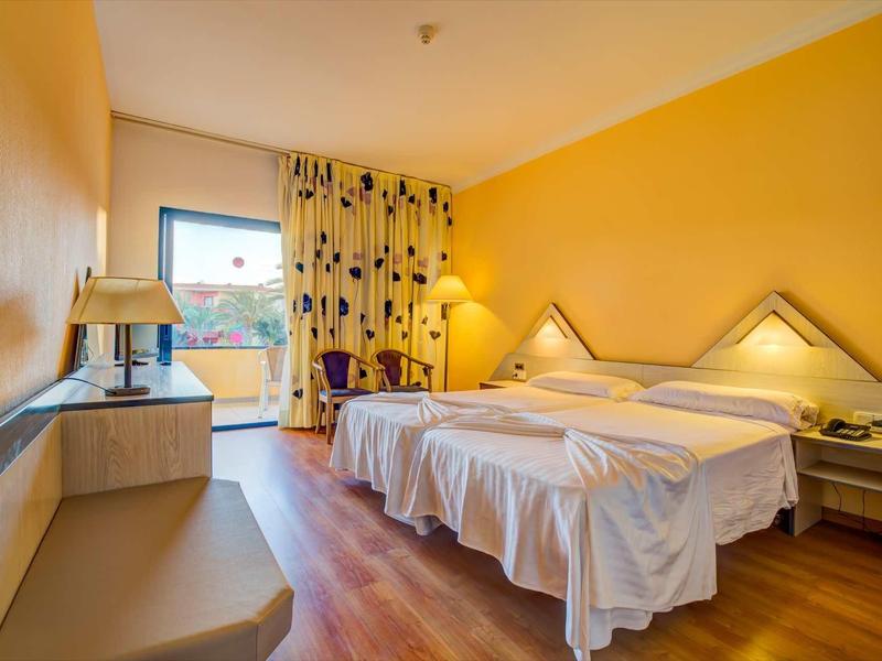 Hotelový pokoj se dvěma postelemi, žlutými zdmi a oknem s závěsy.