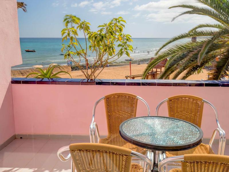 Balkon s kulatým stolem a židlemi, výhled na pláž, moře a palmy za slunečného dne.