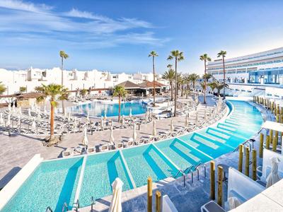 Piscine d'hôtel moderne avec chaises longues et palmiers sous un ciel bleu.