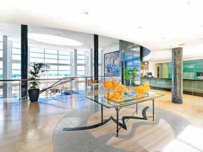 Hall d'hôtel lumineux avec murs en verre, art moderne et chaises jaunes autour d'une table en verre.