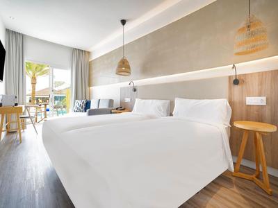 Chambre d'hôtel lumineuse avec lit double, boiseries et terrasse donnant sur des palmiers.