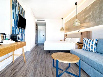 Chambre d'hôtel moderne avec lit double, canapé, sol en bois et éclairage élégant.