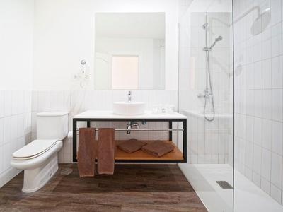 Salle de bain propre et moderne avec toilettes blanches, lavabo, douche et sol en carrelage bois.