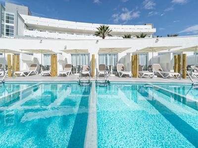 Piscine moderne d'hôtel avec transats et parasols sous un ciel bleu.
