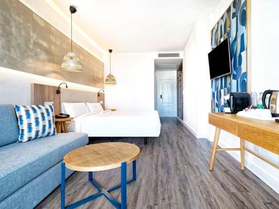 Chambre d'hôtel moderne avec lit double, canapé bleu et sol en bois.