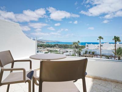 Balcon avec deux chaises et une table donnant sur la piscine de l'hôtel et la mer par une journée ensoleillée.