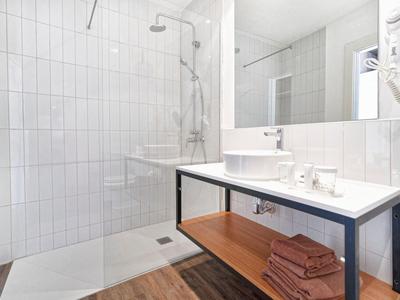 Salle de bain lumineuse avec douche à l'italienne, lavabo moderne et serviettes sur étagère en bois.
