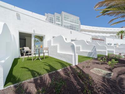 Terrasses d'hôtel blanches avec gazon artificiel et sièges sous un ciel bleu clair.
