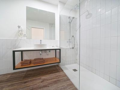 Salle de bain moderne avec douche carrelée blanche, grand miroir et sol en bois.