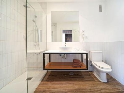 Salle de bain moderne avec douche, lavabo, toilettes et sol en bois dans un hôtel.