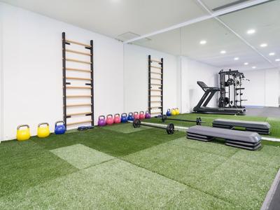Salle de sport avec sol en gazon artificiel, haltères, kettlebells, tapis de course et mur miroir.