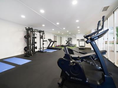 Salle de sport d'hôtel moderne avec équipements, tapis et intérieur lumineux et spacieux.