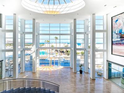 Hall d'hôtel lumineux avec grandes fenêtres donnant sur la piscine et la mer.