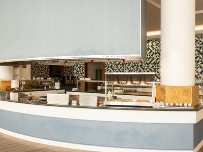 Bar d'hôtel moderne avec comptoir blanc, colonnes hautes et décoration murale noire élégante.