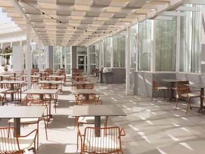 Espace extérieur d'hôtel vide avec tables et chaises sur une terrasse sous un toit en pergola.