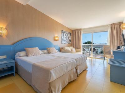 Bright hotel room with two single beds, blue furniture, and balcony view.