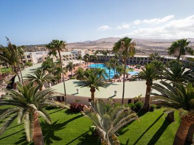 Hotel complex with pool, palm trees, and scenic view of surrounding landscape under clear sky.