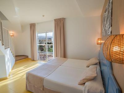 Bright hotel room with two beds, a window with outdoor view, and warm lighting.