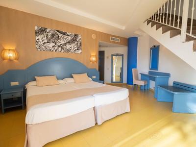Bright hotel room with large double bed, blue furniture, and staircase in the background.