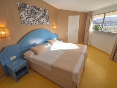 Brightly decorated hotel room with blue headboard, two beds, and large window with landscape view.