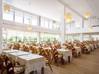 Bright modern dining room with white tables, wooden floors, many chairs, and large windows.