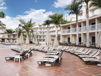 Empty lounge chairs around a hotel pool with palm trees and blue sky.