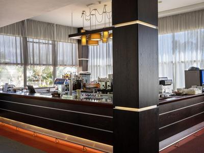 Modern hotel bar area with large windows, curtains, and stylish lighting.