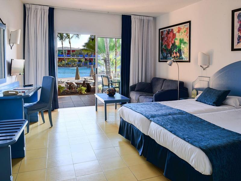 Moderní hotelový pokoj s manželskou postelí a výhledem na bazén a zahradu.