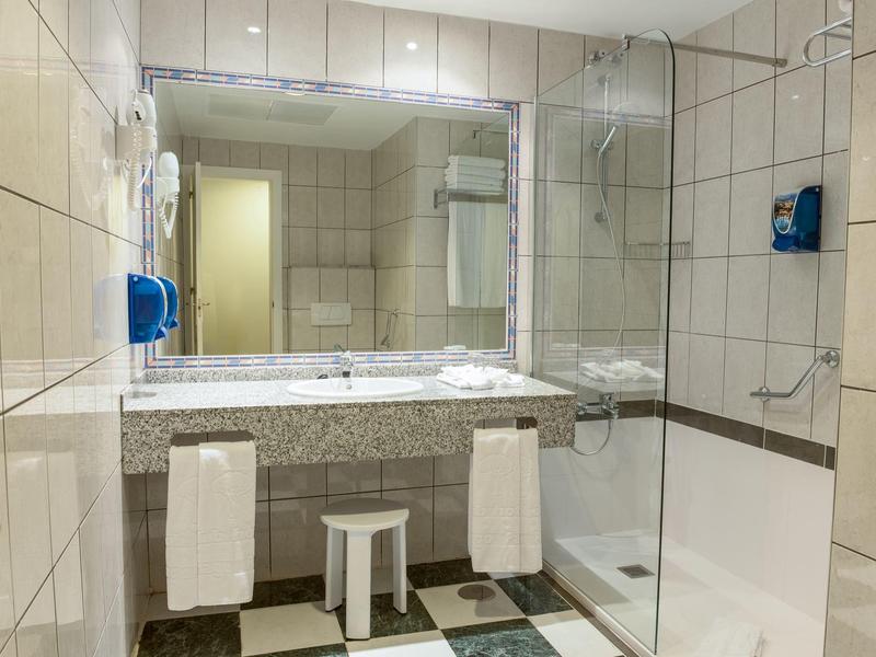 Světla koupelna s velkou zrcadlovou stěnou, sprchovým koutem a mramorovým umyvadlem se dvěma ručníky.