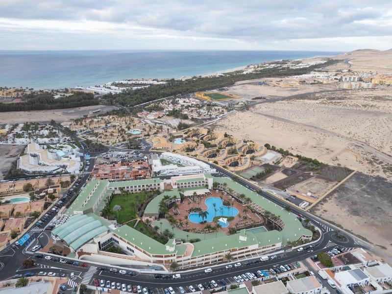 Letecký pohled na přímořské letovisko s bazénem a hotely, obklopené pouští a mořem v pozadí.