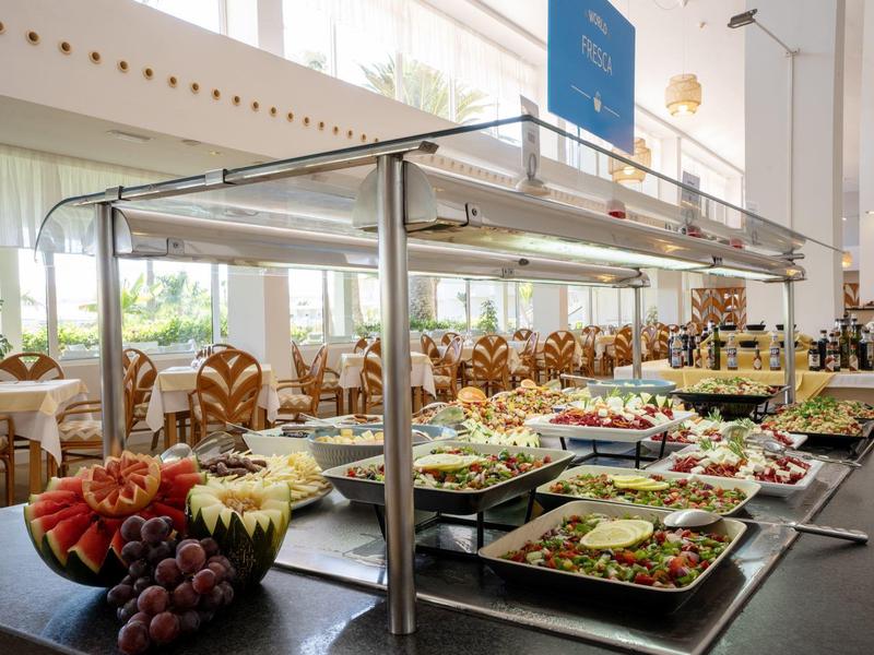 Bufet s různými čerstvými ovocemi, saláty a dalšími pokrmy ve světlé jídelně.