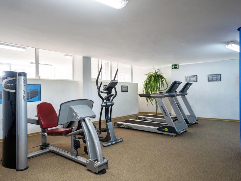 Moderní fitness místnost s běžeckými pásy, rotopedem a eliptickým trenažérem v světlém prostoru.