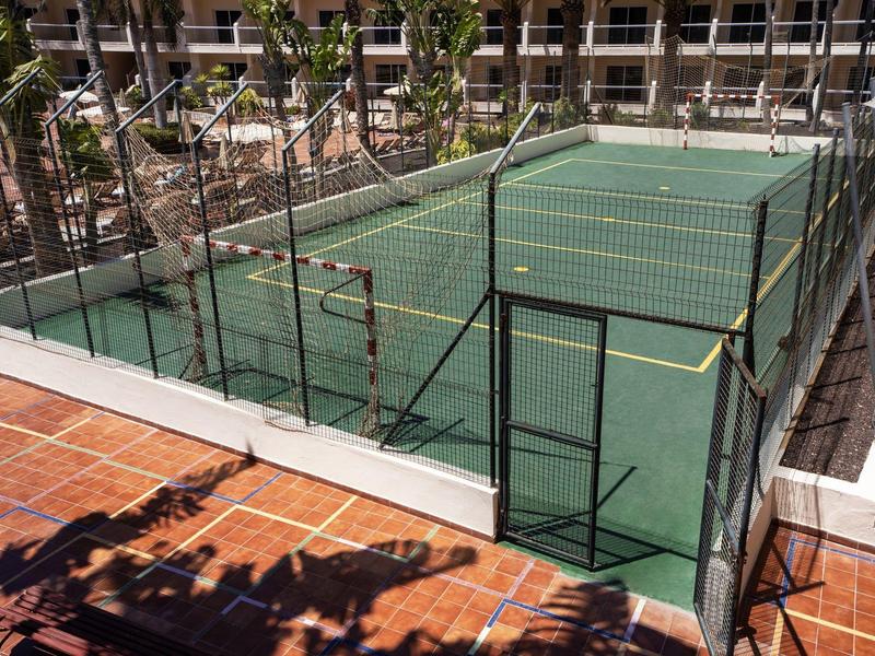 Malý venkovní tenisový kurt s okolní sítí v hotelovém areálu.