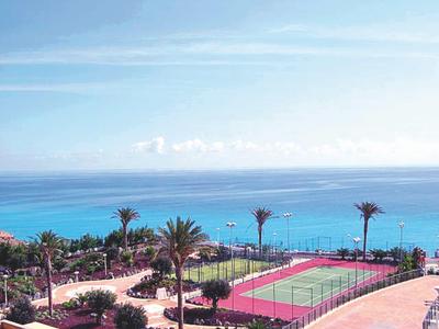 Blick auf einen Tennisplatz am Meer mit Palmen und blauem Himmel im Hintergrund