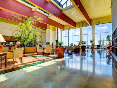 Prostorná hotelová hala s rostlinami a sezením u velkých oken.