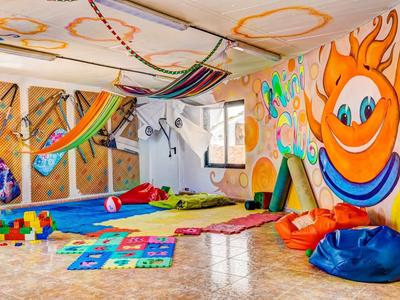 Barevná dětská herna s podložkami, hračkami a veselým slunečním nástěnným malbám.