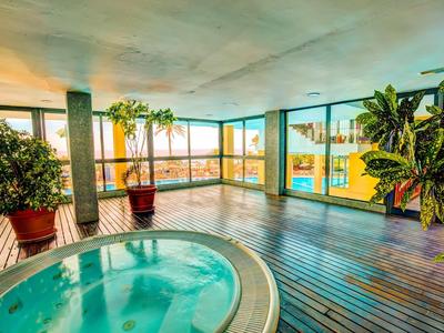 Krytá oblast s vířivkou s dřevěnou podlahou a velkými panoramatickými okny s výhledem na palmy.