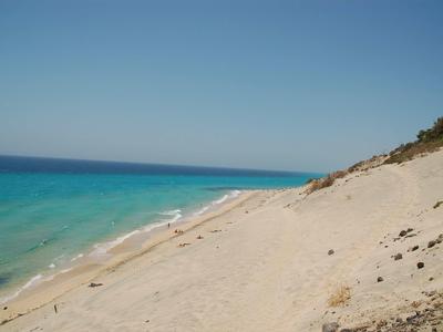 Pláž s jemným pískem a průzračnou tyrkysovou vodou pod modrou oblohou.