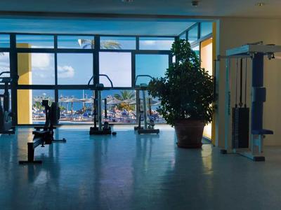 Helles Fitnessstudio mit großen Fenstern und Blick auf eine Stadtlandschaft.