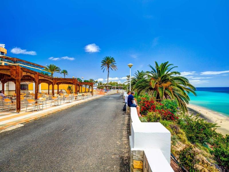 Silnice u pláže s palmami, pergolami a jasně modrou oblohou