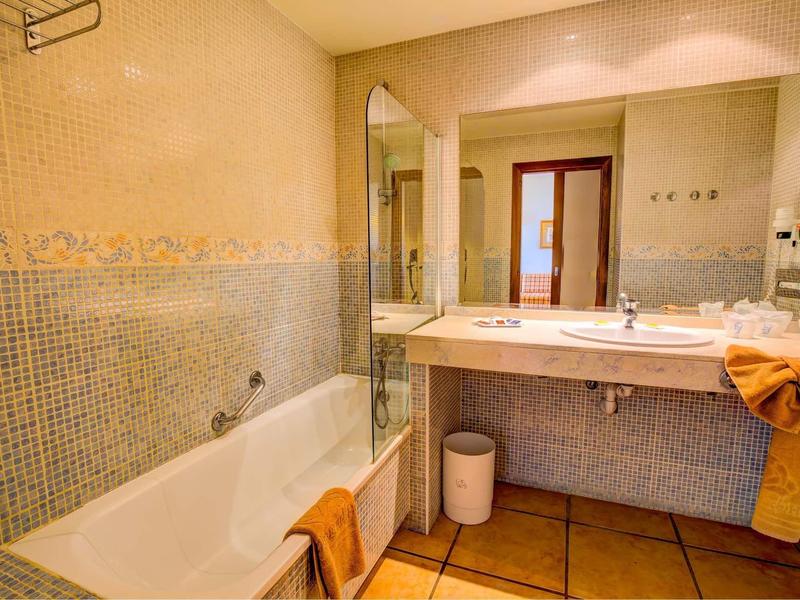 Světlá koupelna s vanou, velkým zrcadlem, umyvadlem a oranžovou dekorací ručníků.