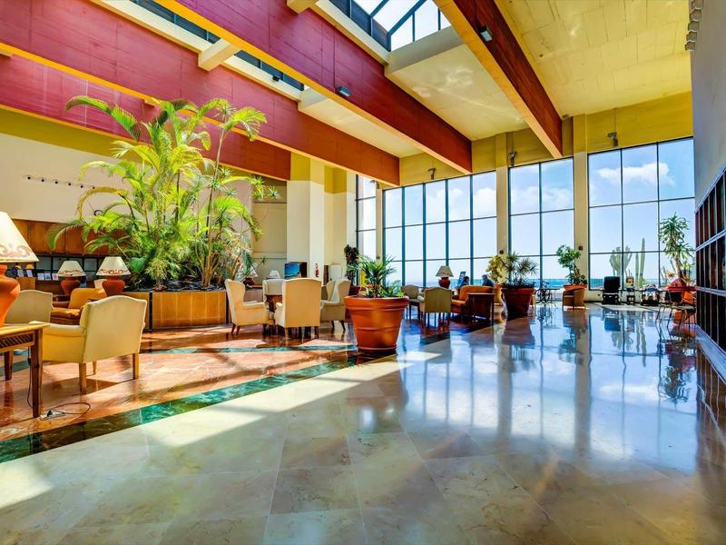 Prostorná hotelová hala s rostlinami a sezením u velkých oken.