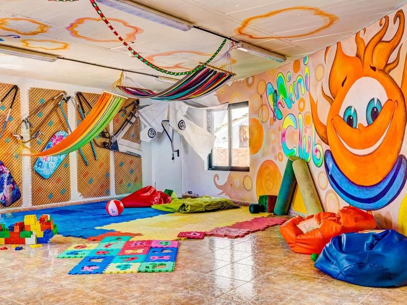 Barevná dětská herna s podložkami, hračkami a veselým slunečním nástěnným malbám.