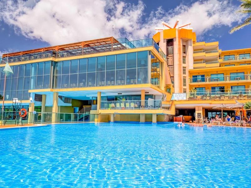 Moderní hotelový komplex s velkým venkovním bazénem pod modrou oblohou.