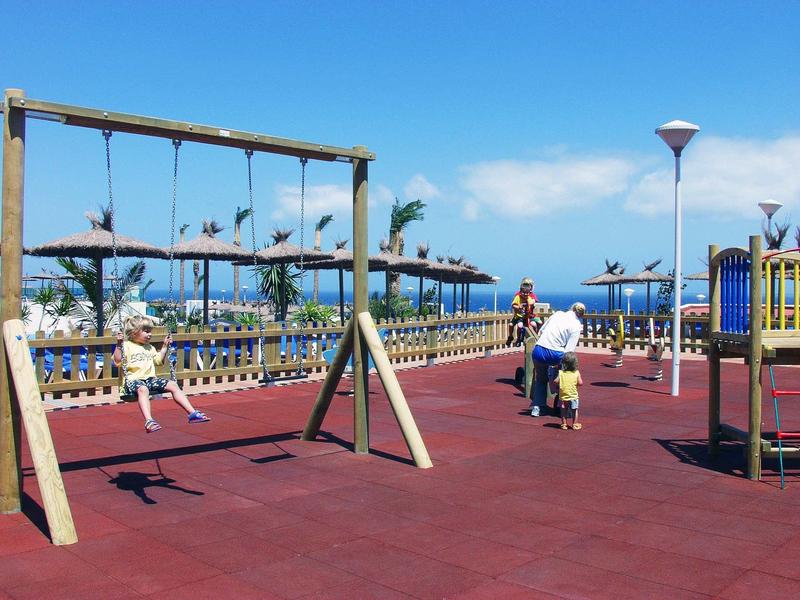 Venkovní restaurace s dřevěnými střechami, stoly a židlemi za slunečného počasí a modré oblohy.