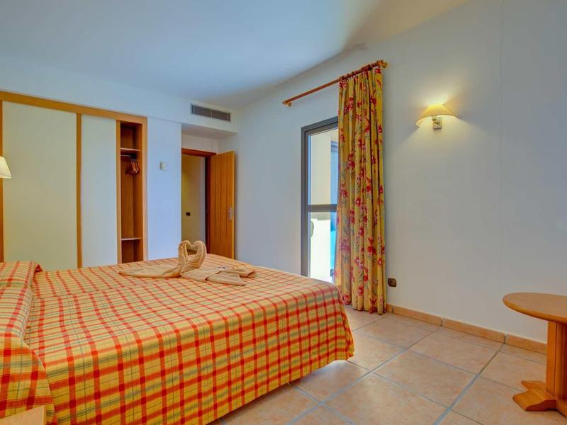 Hotelový pokoj se dvěma jednolůžky, okno se závěsem a jednoduchou dřevěnou výzdobou.