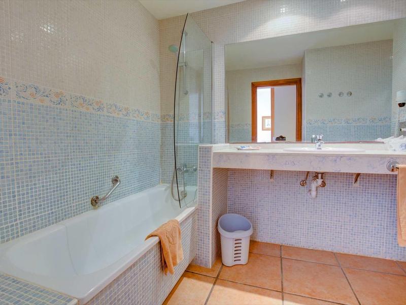 Světlá koupelna s vanou, velkým zrcadlem a umyvadlem s ručníky.